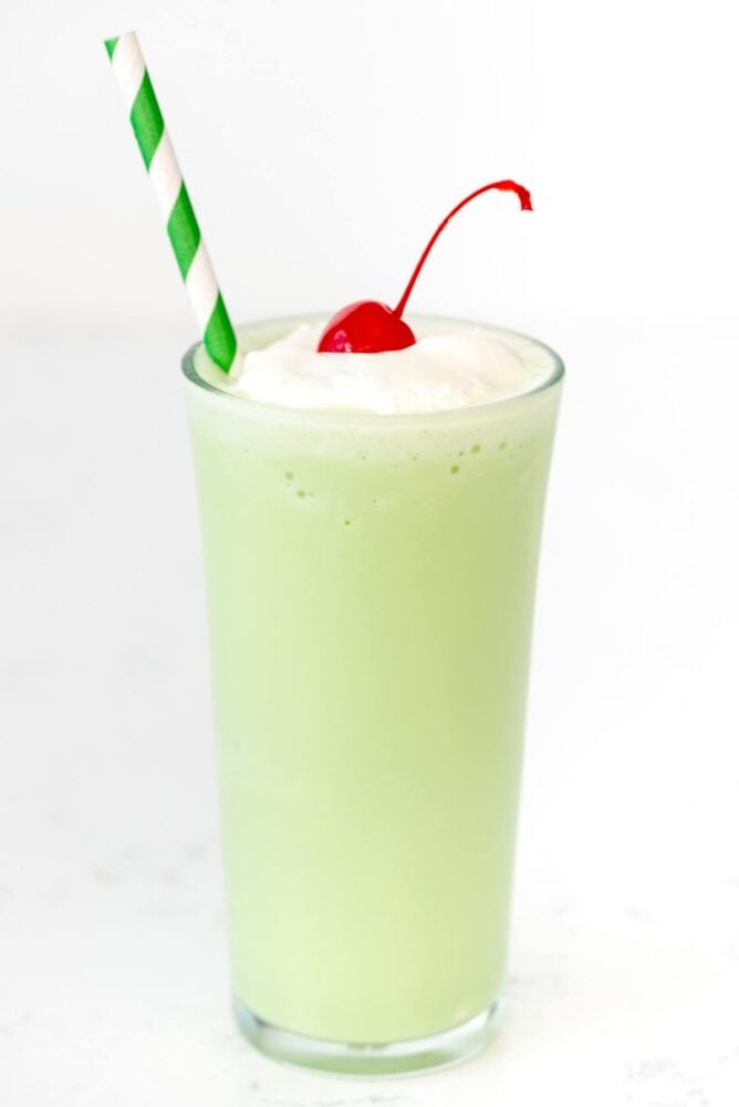 Copycat Mint Shamrock Shake in tall glass with a straw and a cherry