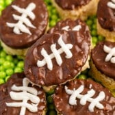 mini Rice Krispie treats in the shape on footballs with brown and white frosting on top to resembles a football on a field.