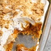 dessert with white cream and graham cracker crumbs on top in a clear pan.